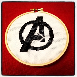 Avengers logo cross-stitched in black and framed in a wooden hoop.