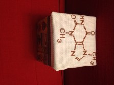 Image of the top and side of a box with the molecular structure of chocolate cross-stitched on the top.