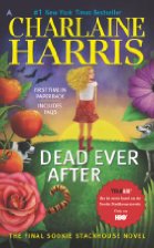 A blonde woman stands among flowers and tomatoes with the sun either setting or rising behind her.