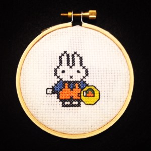 A cross stitch of a bunny holding a basket of carrots