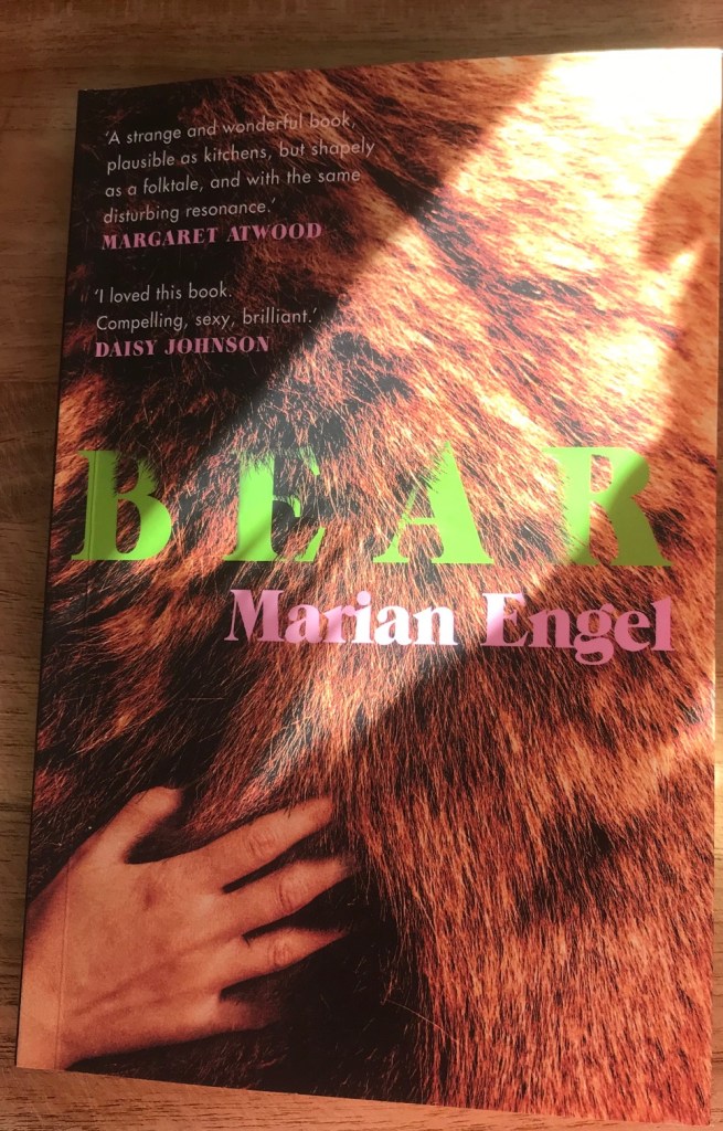 Photo of a physical book cover. The word BEAR in neon green font is on top of the coat of a bear with a woman's hand running through the fur.